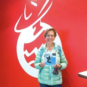 Sarah Chauncey holding a square blue gift book in front of a bright red background